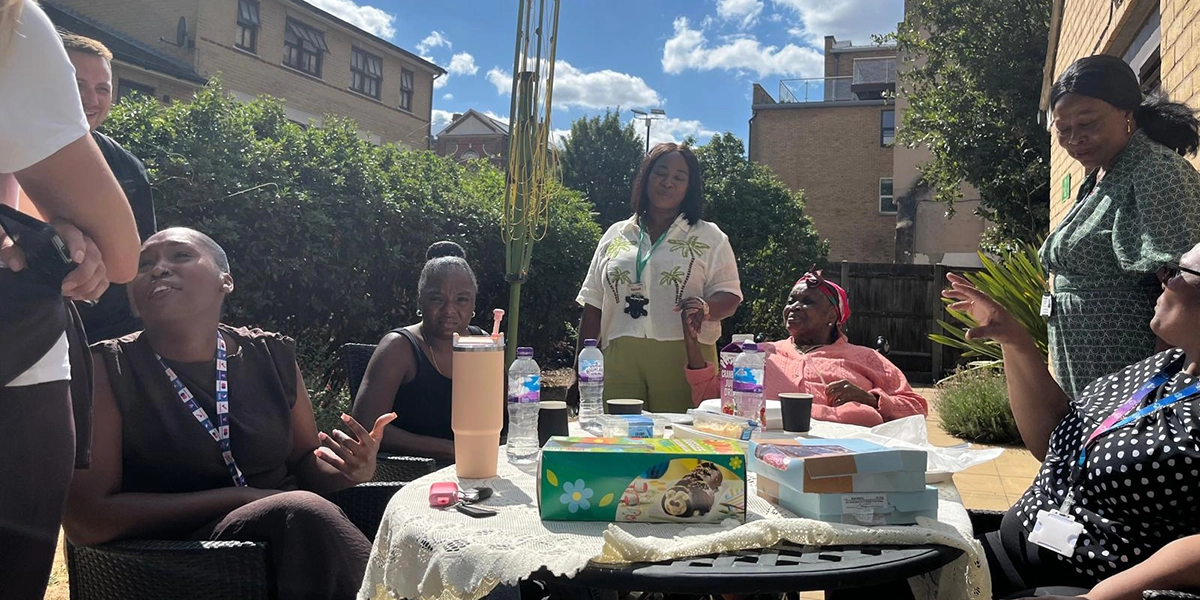 People are sat around a table in the garden smiling and sharing food.