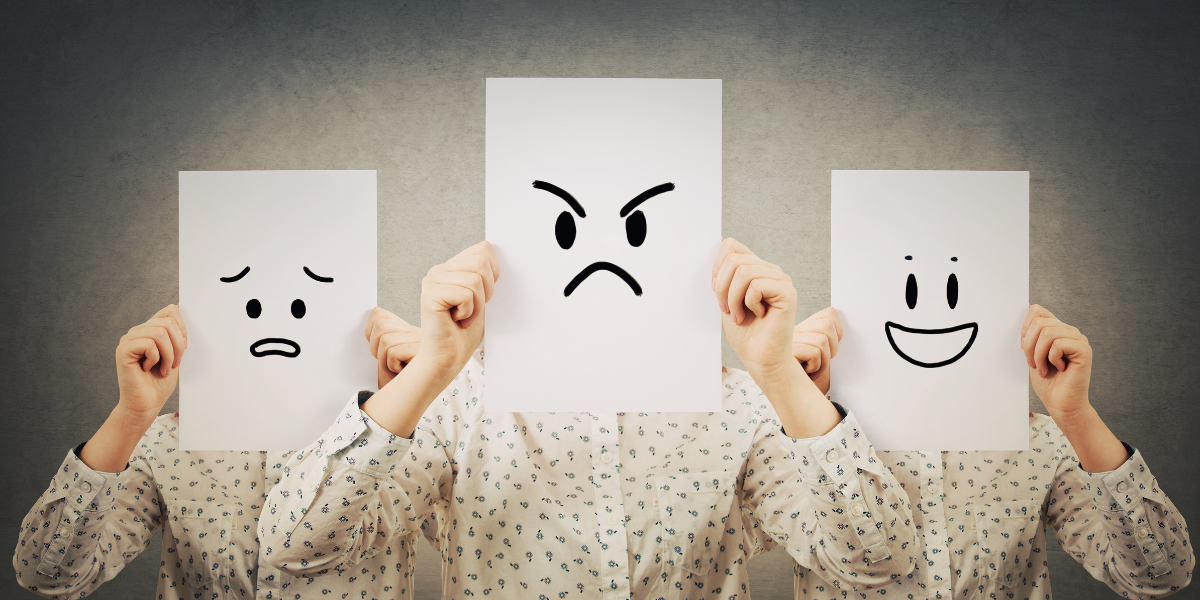 A person holding up pieces of paper with different facial expressions on them.