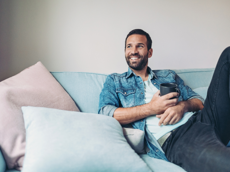 A man relaxes on a couch with a mug of tea. 